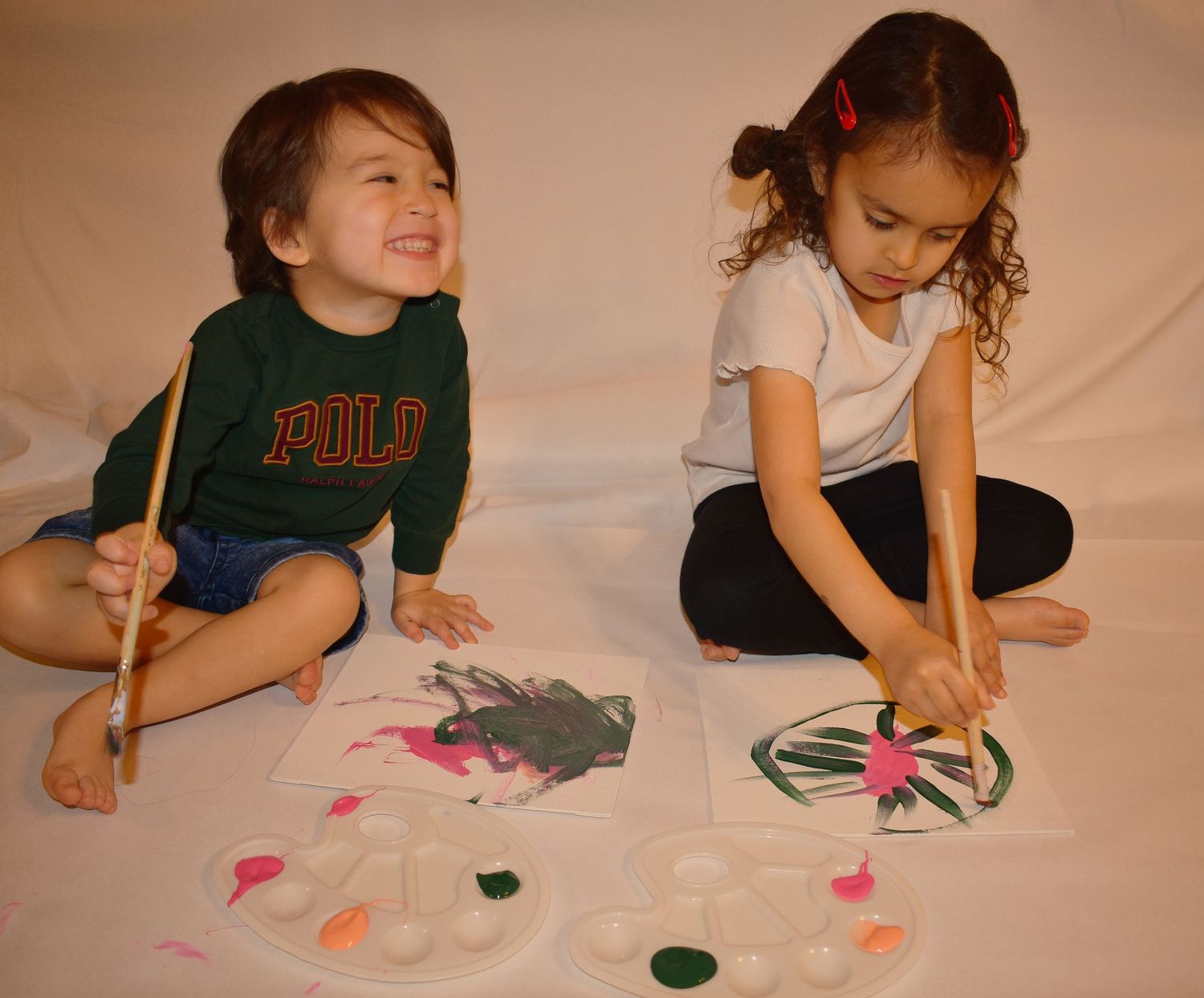 Two children sit on the floor painting together during an art activity.