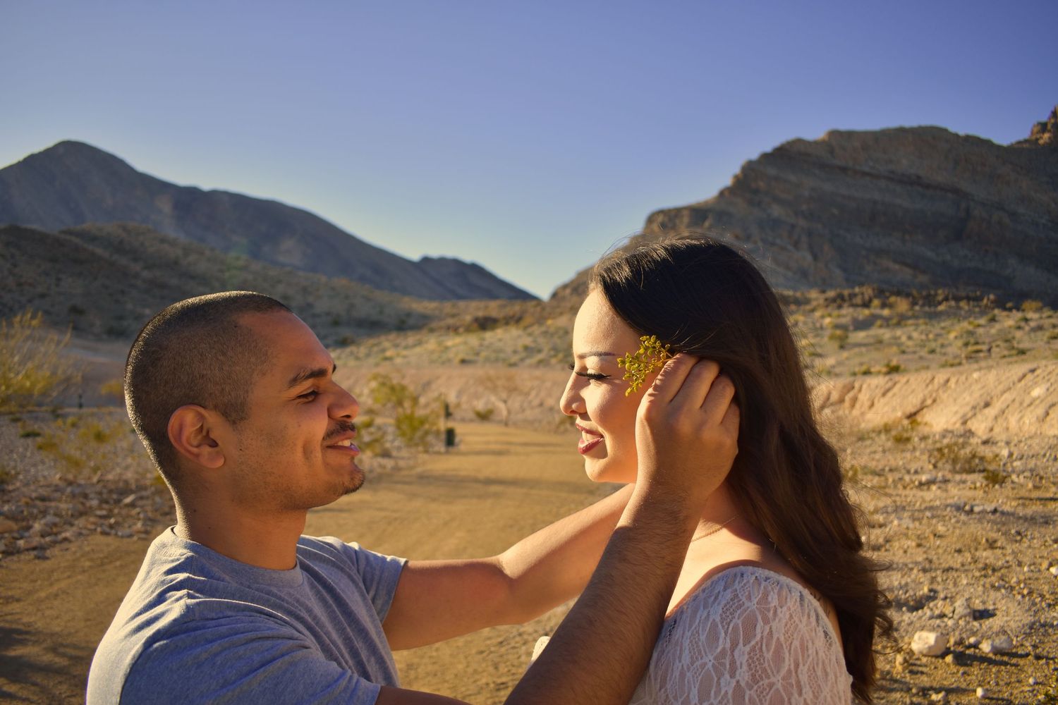 Two people share a romantic moment while hiking through a scenic desert mountain landscape at sunset.