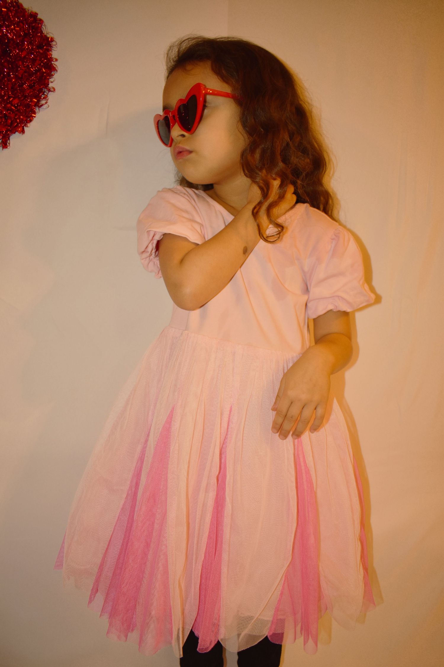 Pink tulle dress twirls in warm lighting against neutral background.