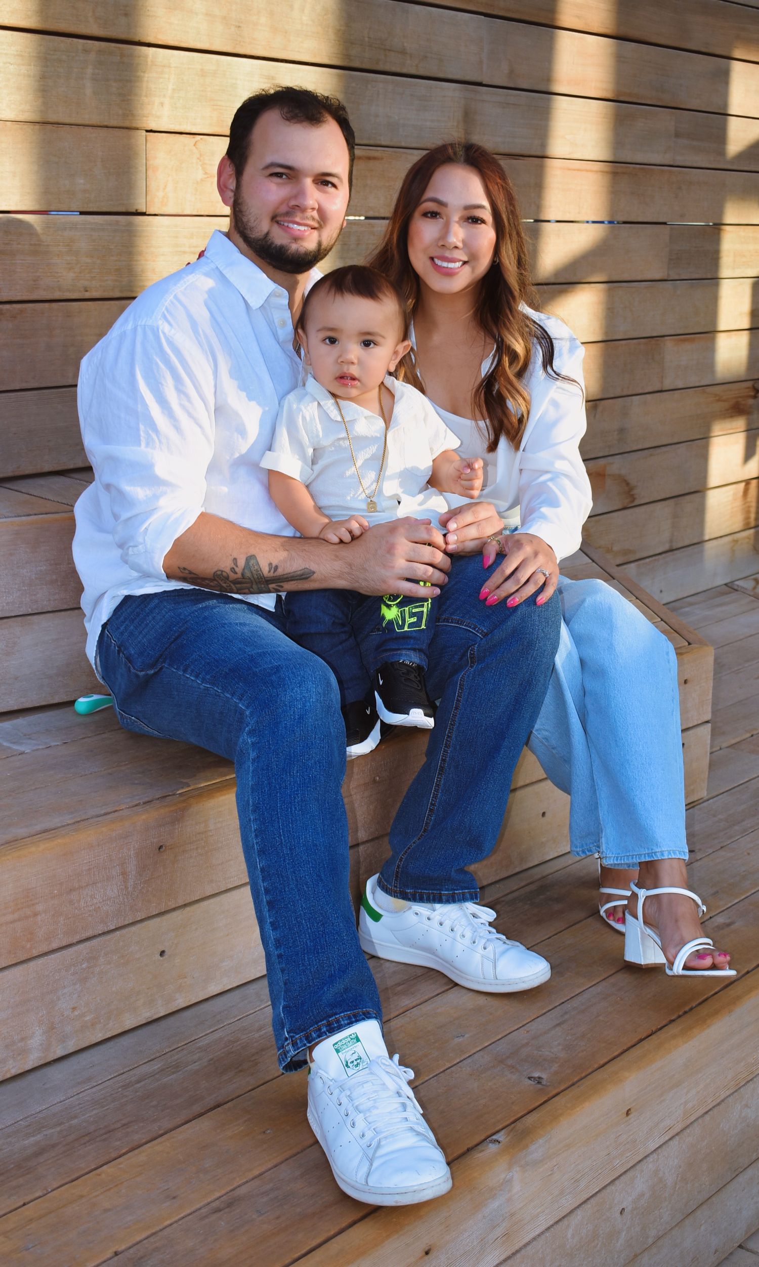 Family in coordinating white and denim outfits sitting on wooden deck.