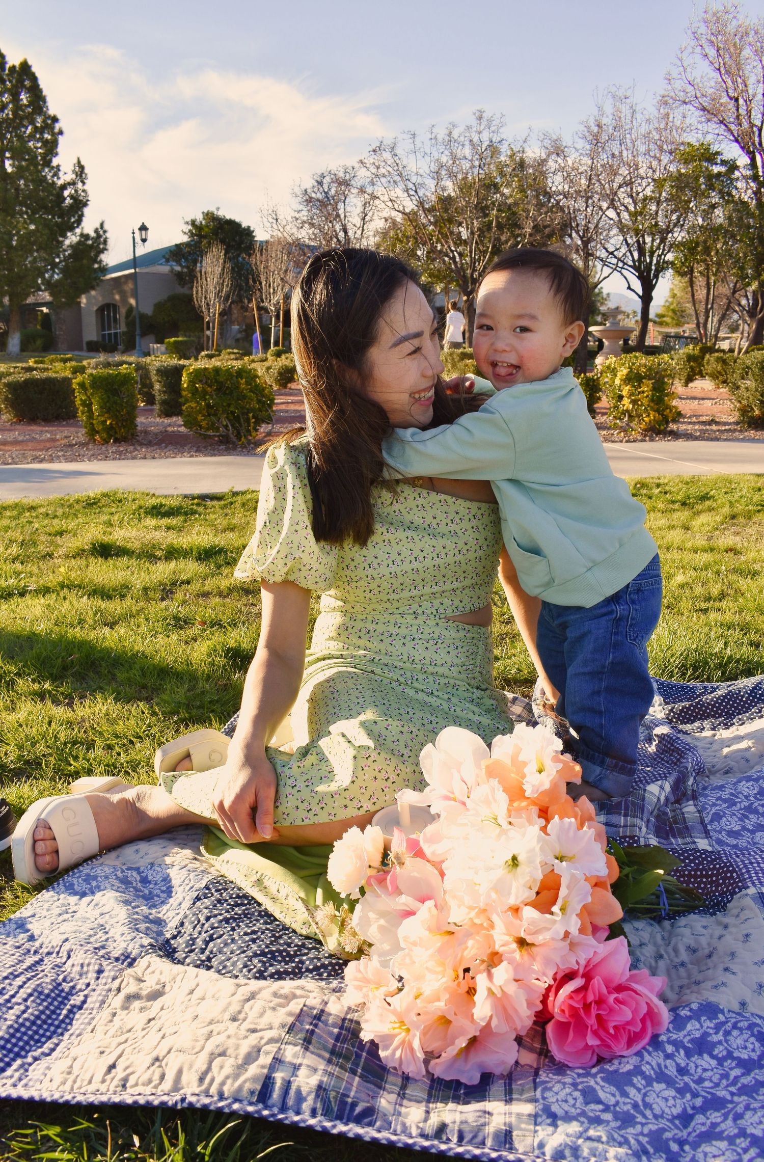 A tender outdoor moment on a blue blanket with peach and pink flowers in the foreground during golden hour.