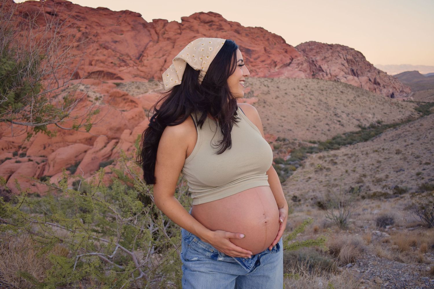A side view maternity portrait with red rock mountains in the desert background.