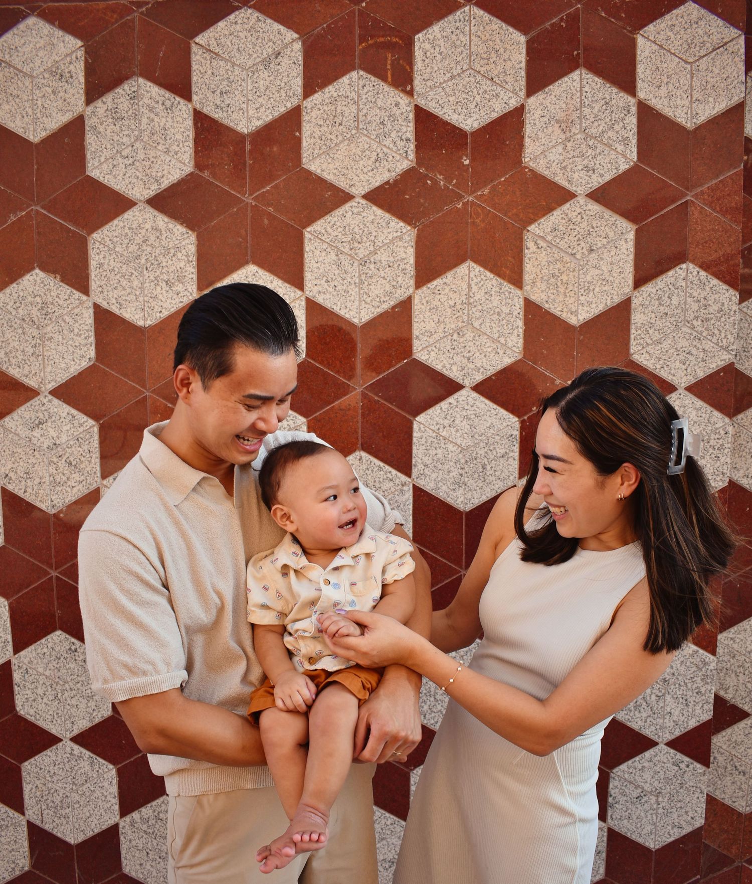Family portrait against geometric wall pattern showing tender moment with infant.