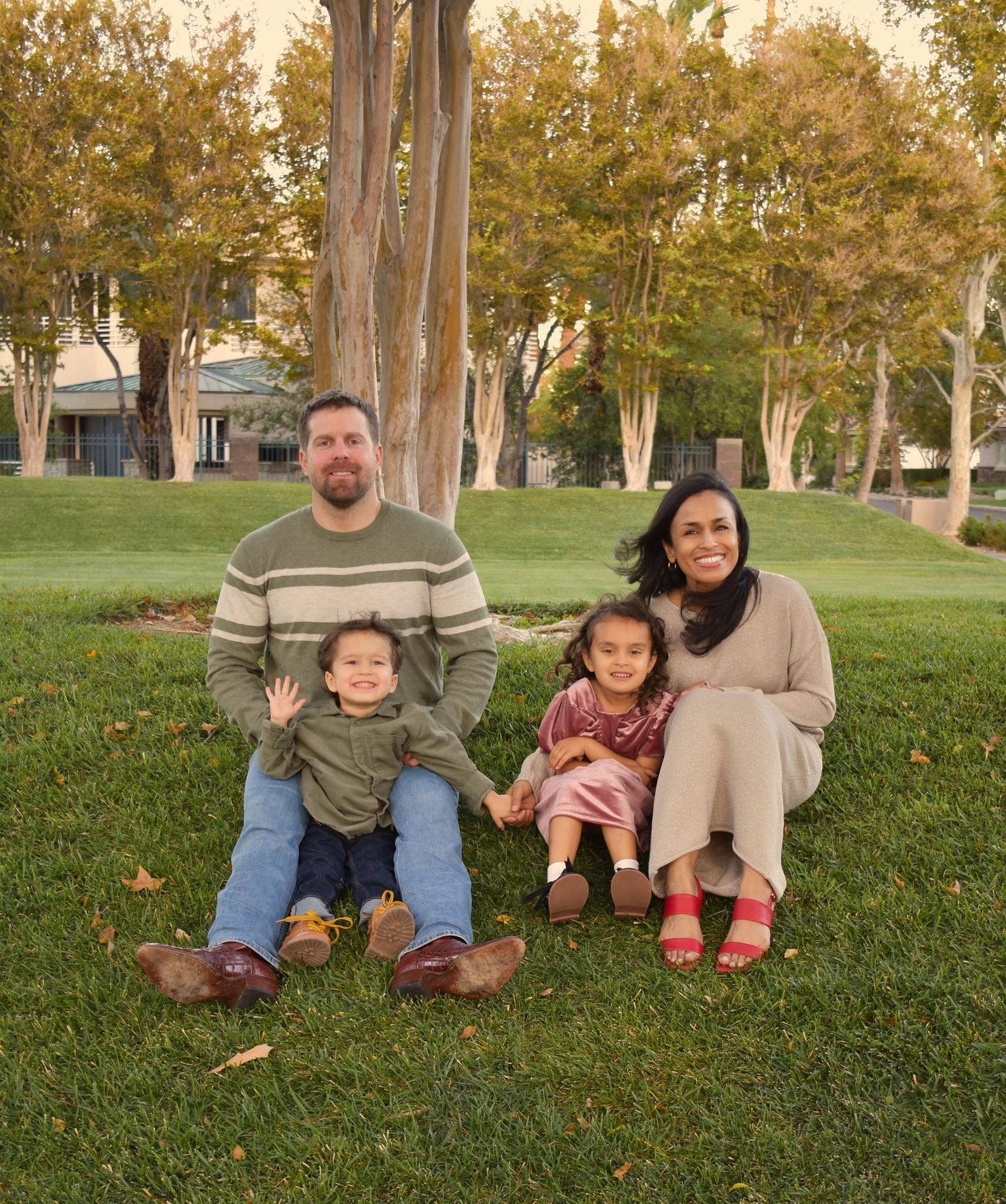 Family sitting together on grass during golden hour in a park setting.