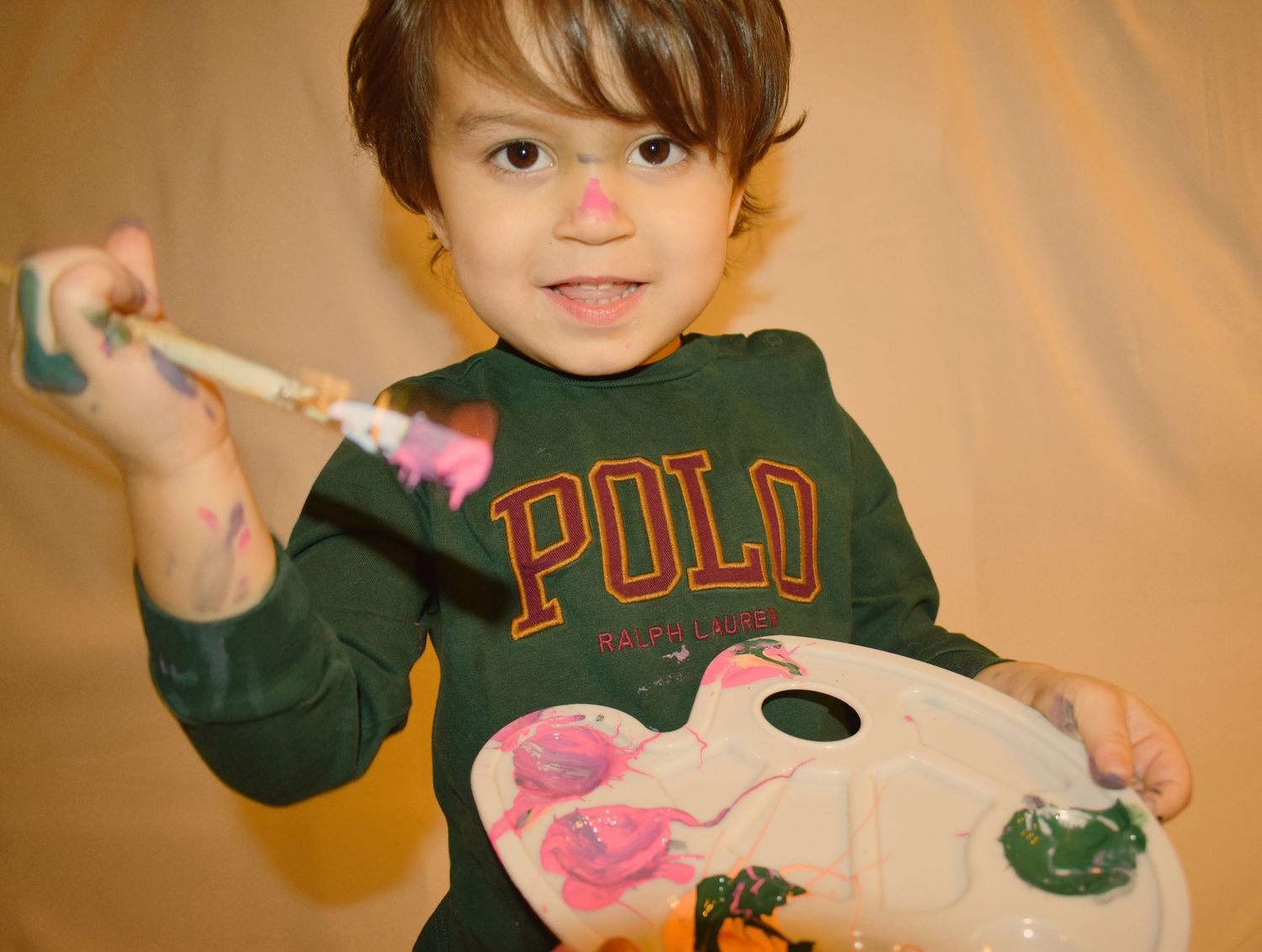Paint-covered hands hold colorful art supplies during creative playtime.