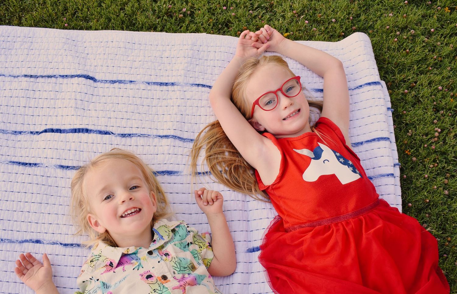 Children resting on a blanket with blue stripes on grass.