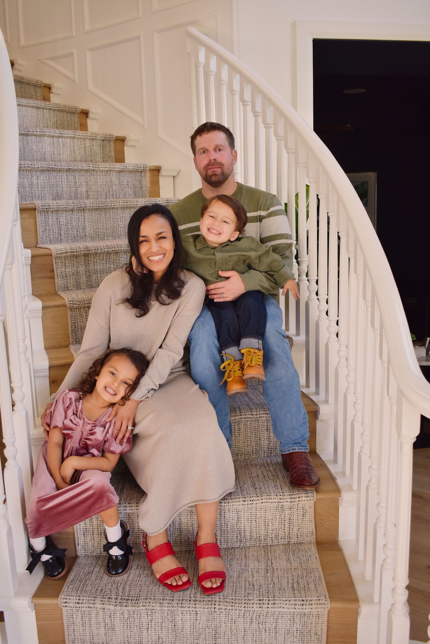Family sits together on carpeted stairs in their home for a casual portrait.