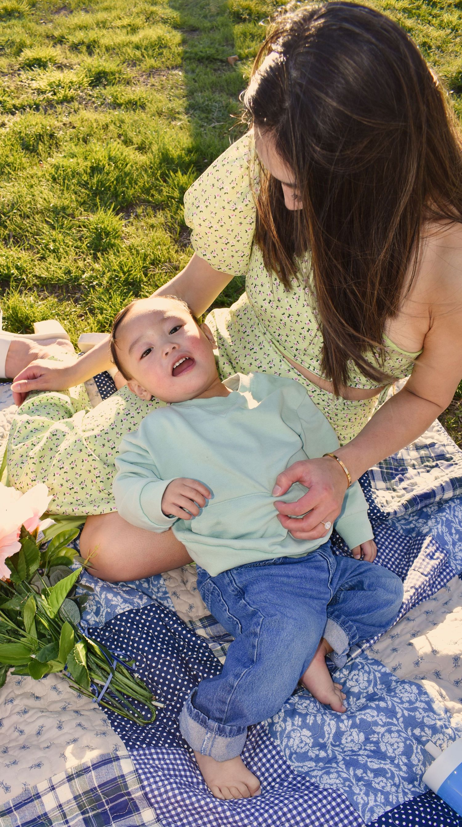 A tender moment of affection between parent and child on a blue checkered blanket in the grass.