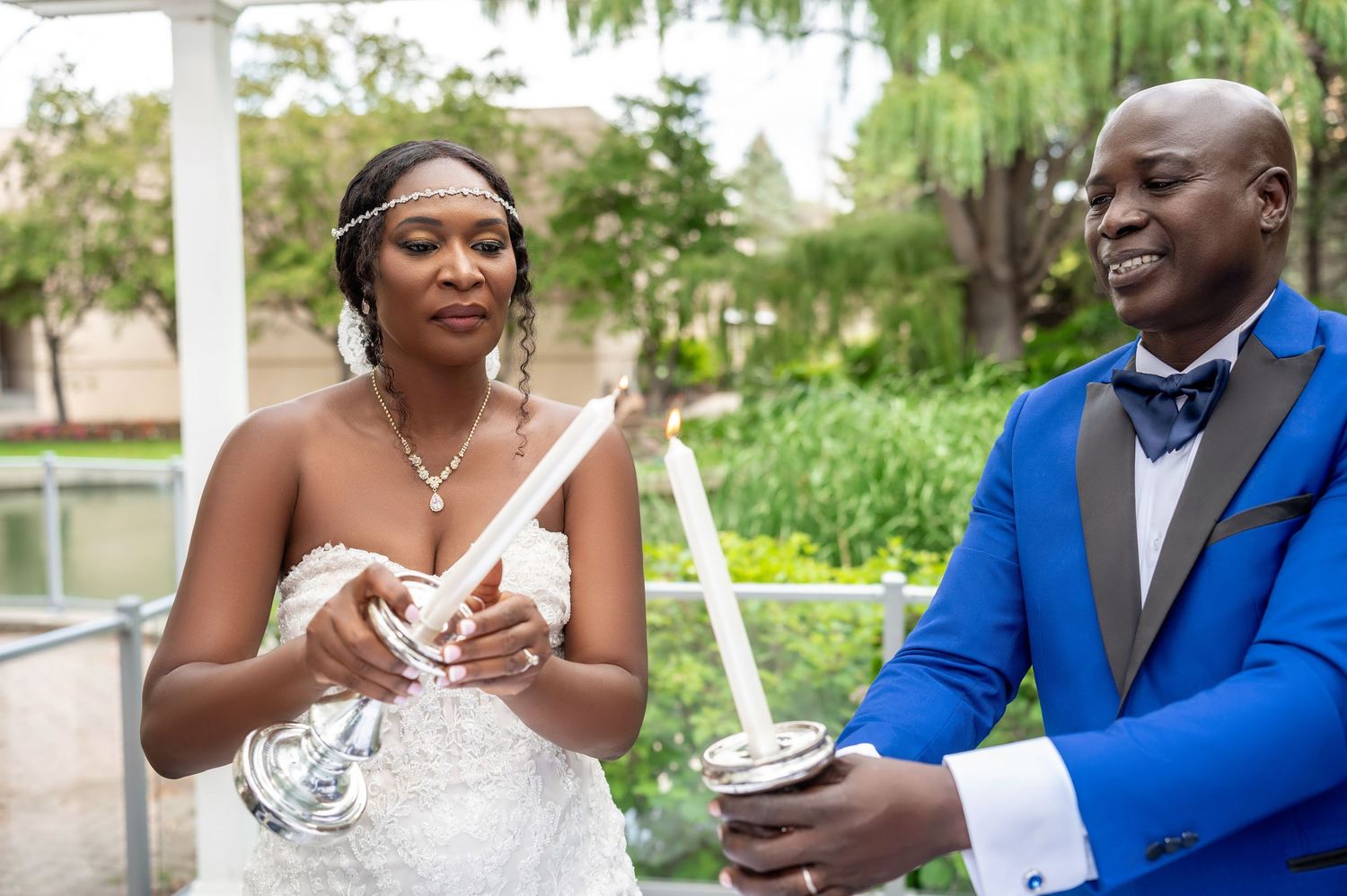 Newlyweds in elegant attire sharing drinks outdoors during wedding celebration.