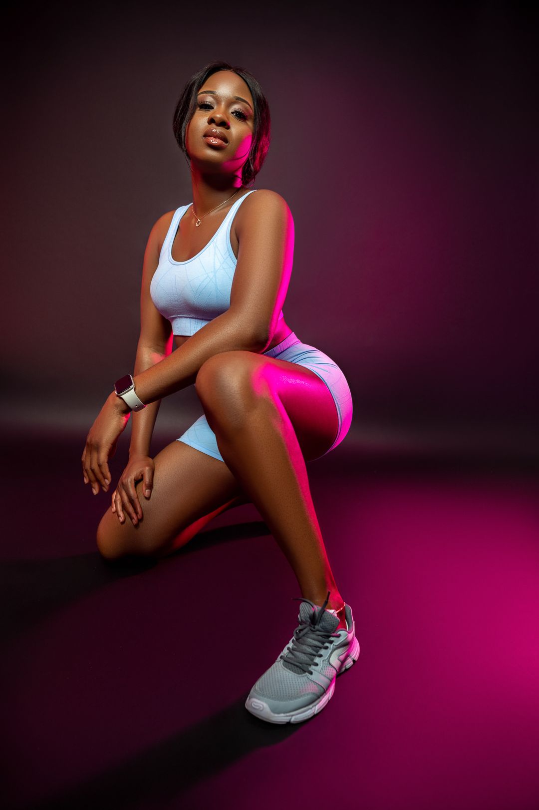 Athletic photoshoot on pink gradient background featuring white sportswear and gray sneakers.