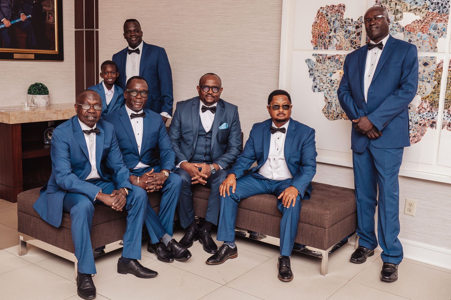 Groomsmen in navy suits gather on brown leather couch for formal wedding portrait.