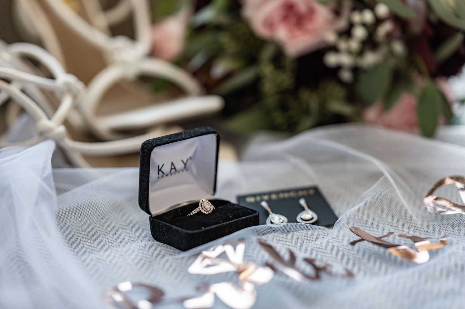 Wedding rings and jewelry box arranged with roses and delicate white fabric.