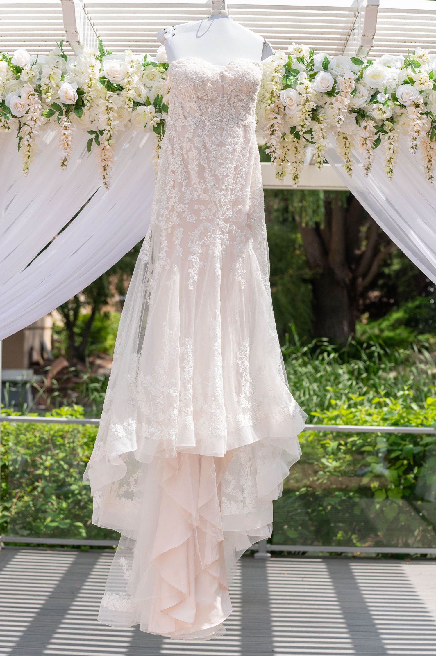 Lace wedding dress with sweetheart neckline displayed against floral arch backdrop.