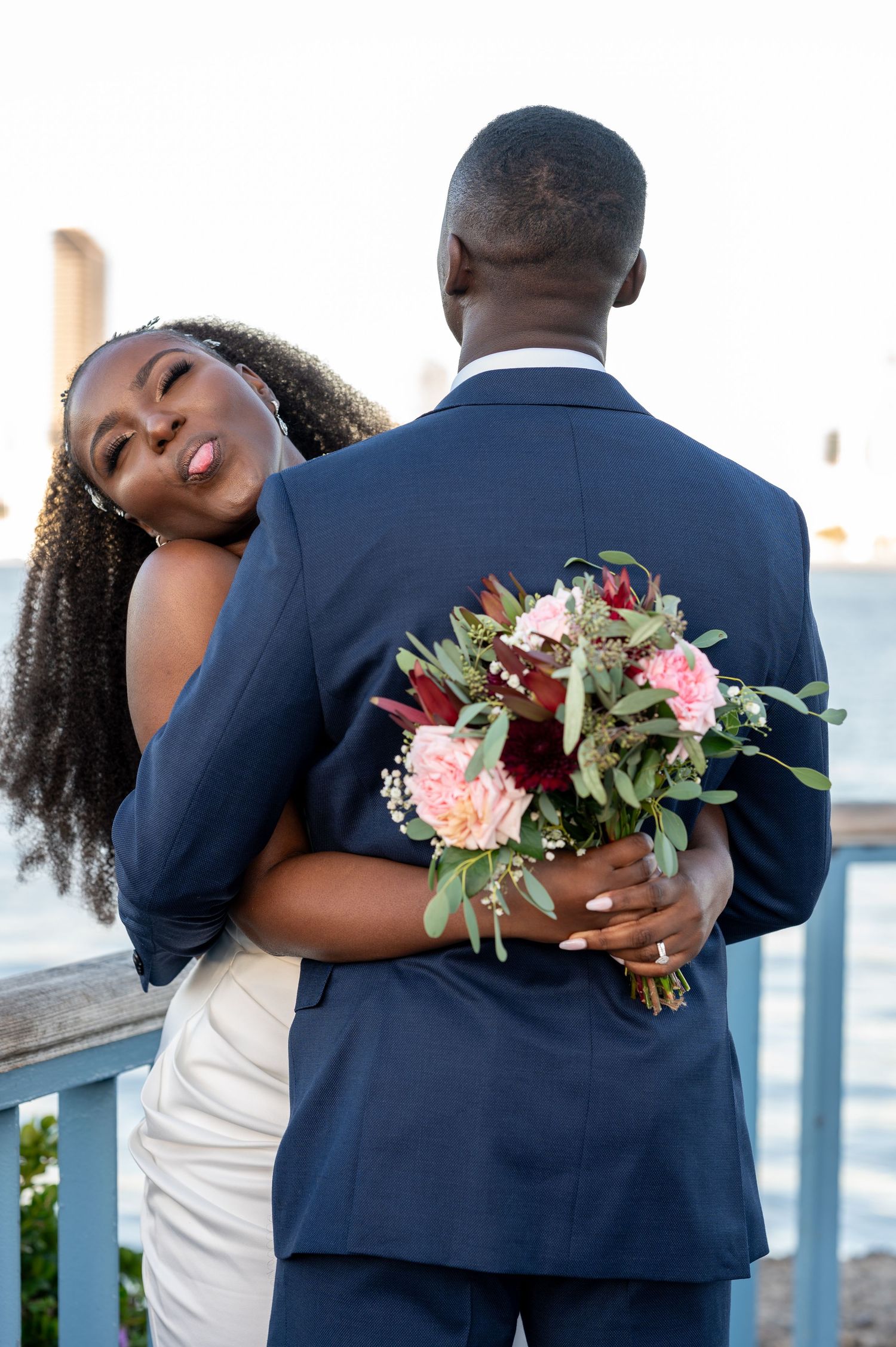 Romantic couple embrace outdoors with pink and burgundy bouquet against blue suit.