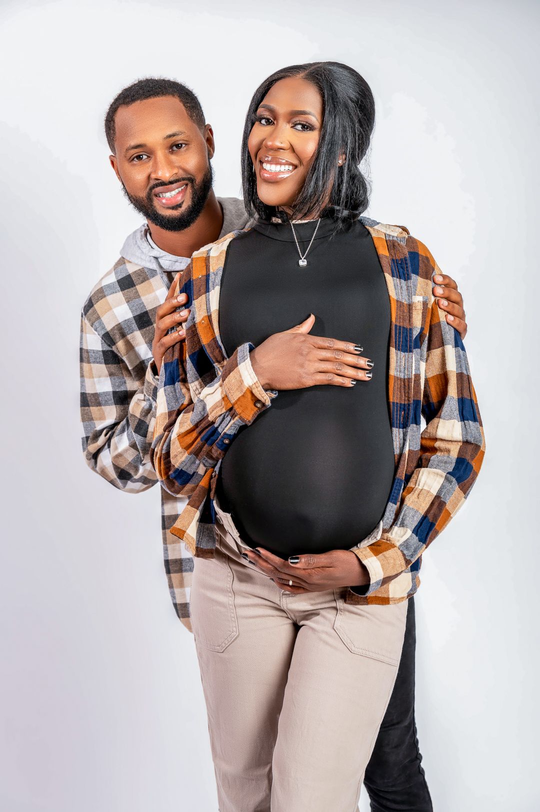 Couple embracing during maternity photoshoot, wearing casual plaid and black outfits.