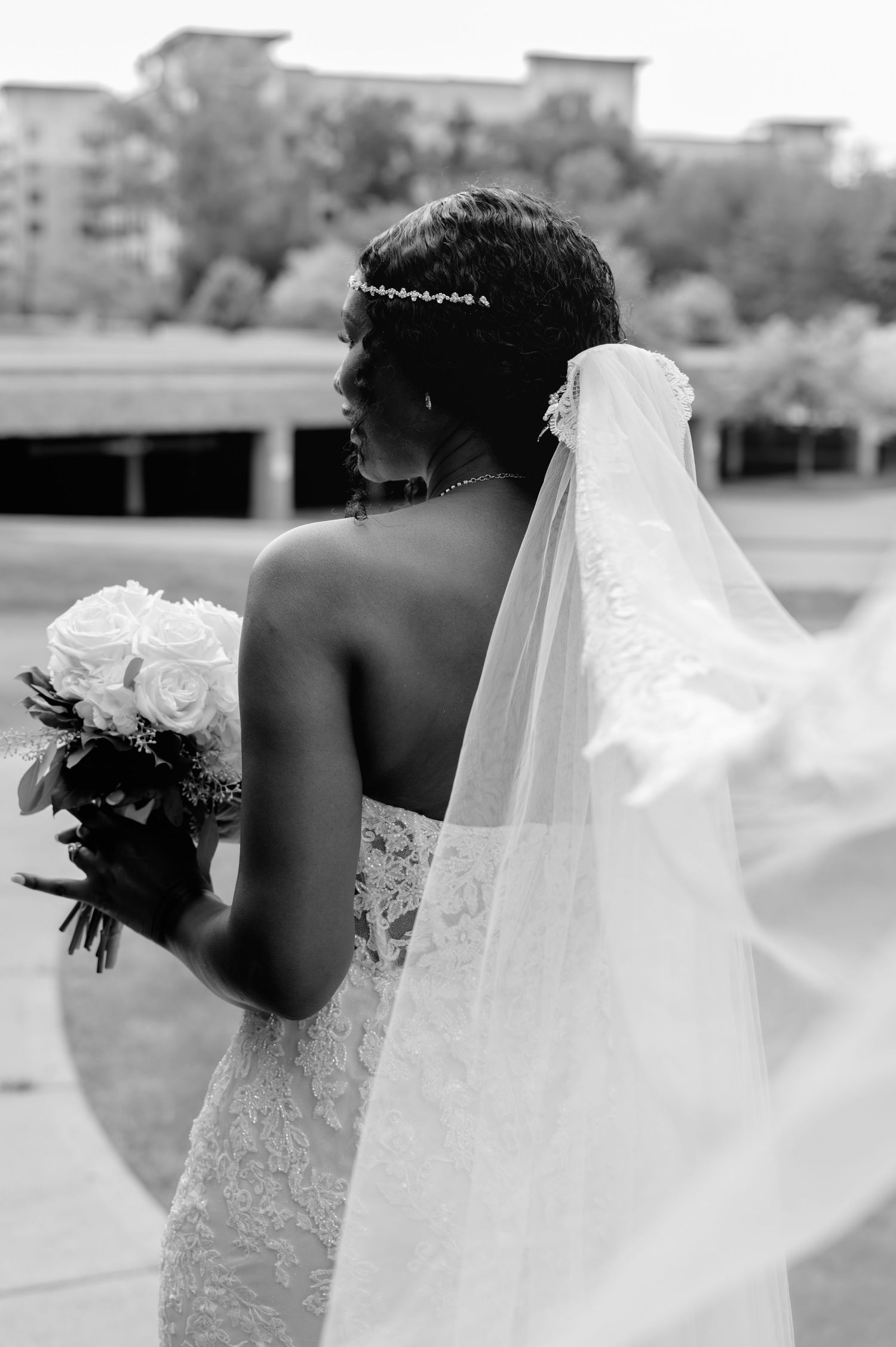 Back view of bride holding roses with flowing veil and detailed lace wedding dress.