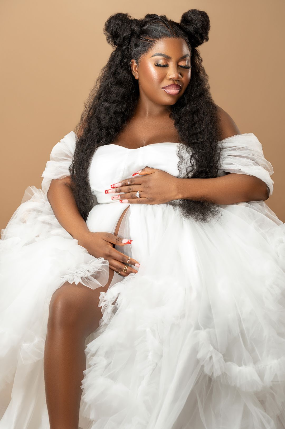 Glamorous maternity photos in flowing white tulle dress against neutral background.