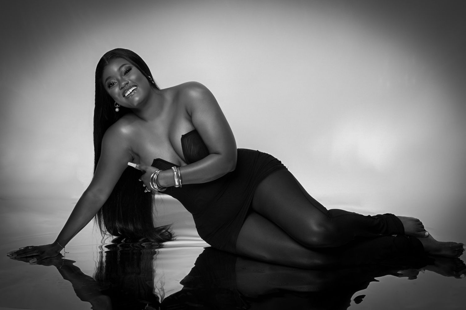 Artistic black and white boudoir photograph with dramatic lighting and reflective surface.