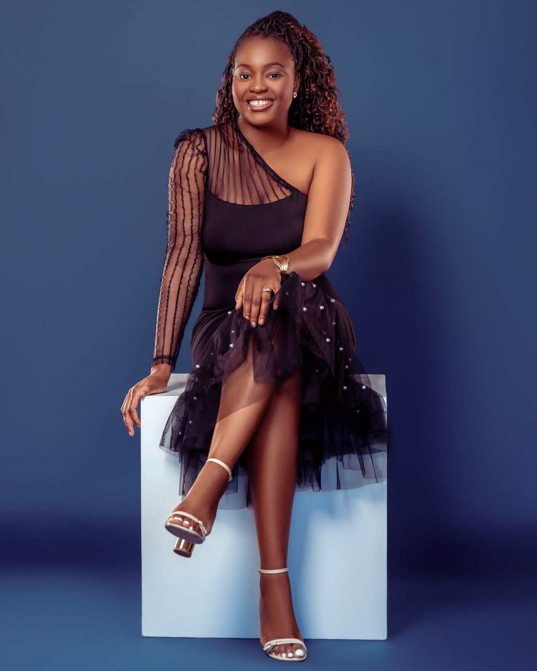 Stylish photoshoot against dark blue backdrop showcasing elegant poses and sparkly dress details.