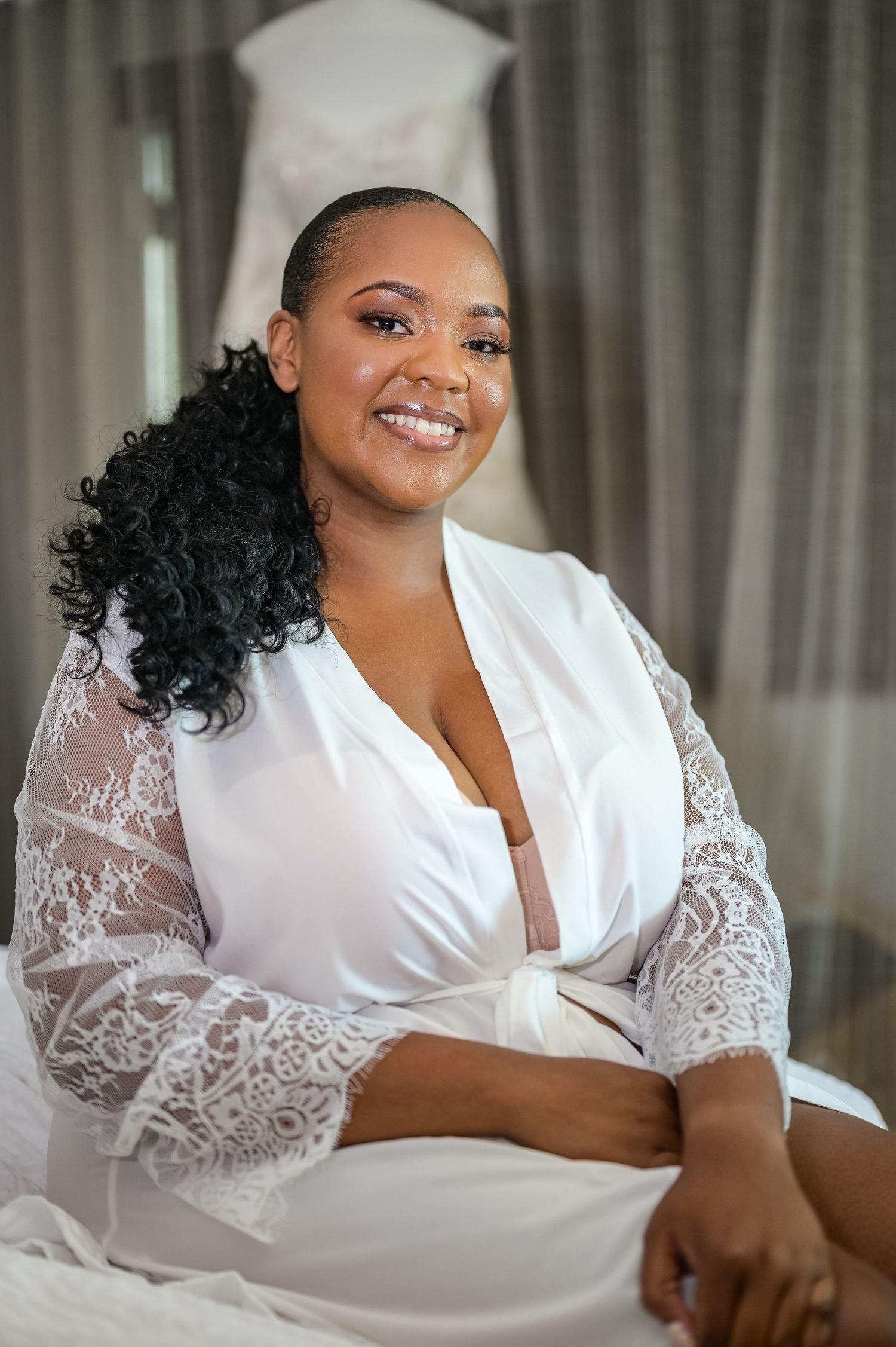 A bridal portrait showing a woman in a white lace robe getting ready for her wedding day.