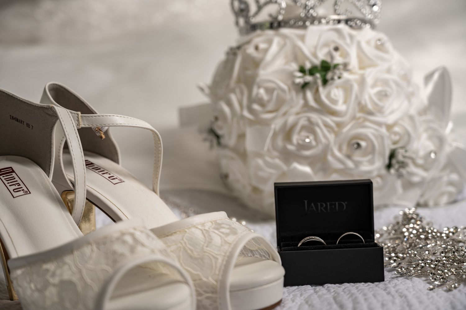 Wedding accessories including white bridal shoes, rings in black box, and floral decorations.