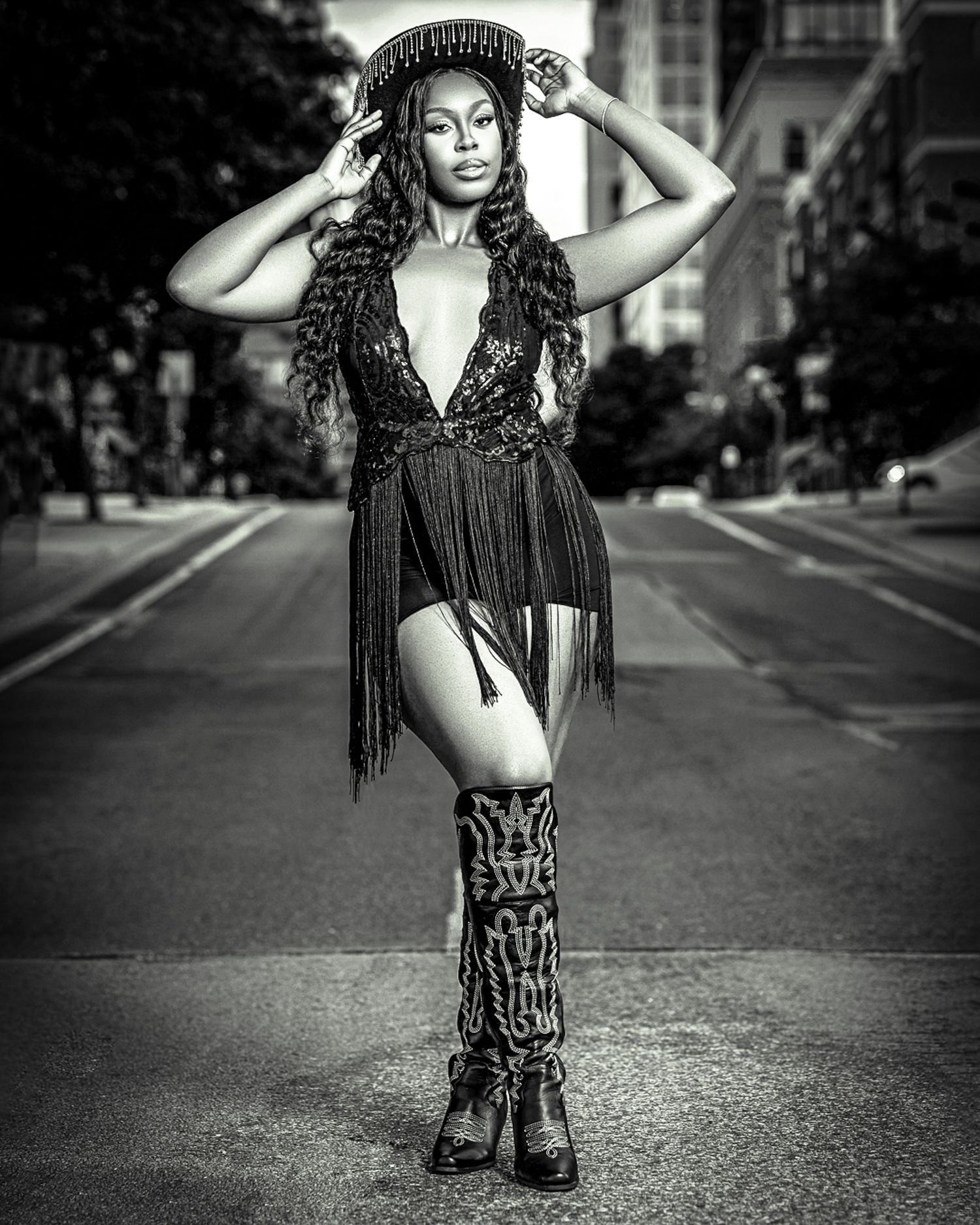 Dramatic street fashion photo of model in fringe dress and boots posing on urban road.