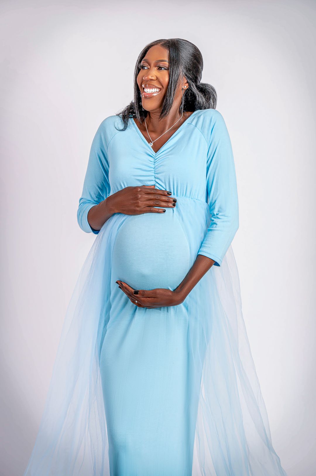 Radiant mother-to-be in turquoise dress smiles during studio maternity session.