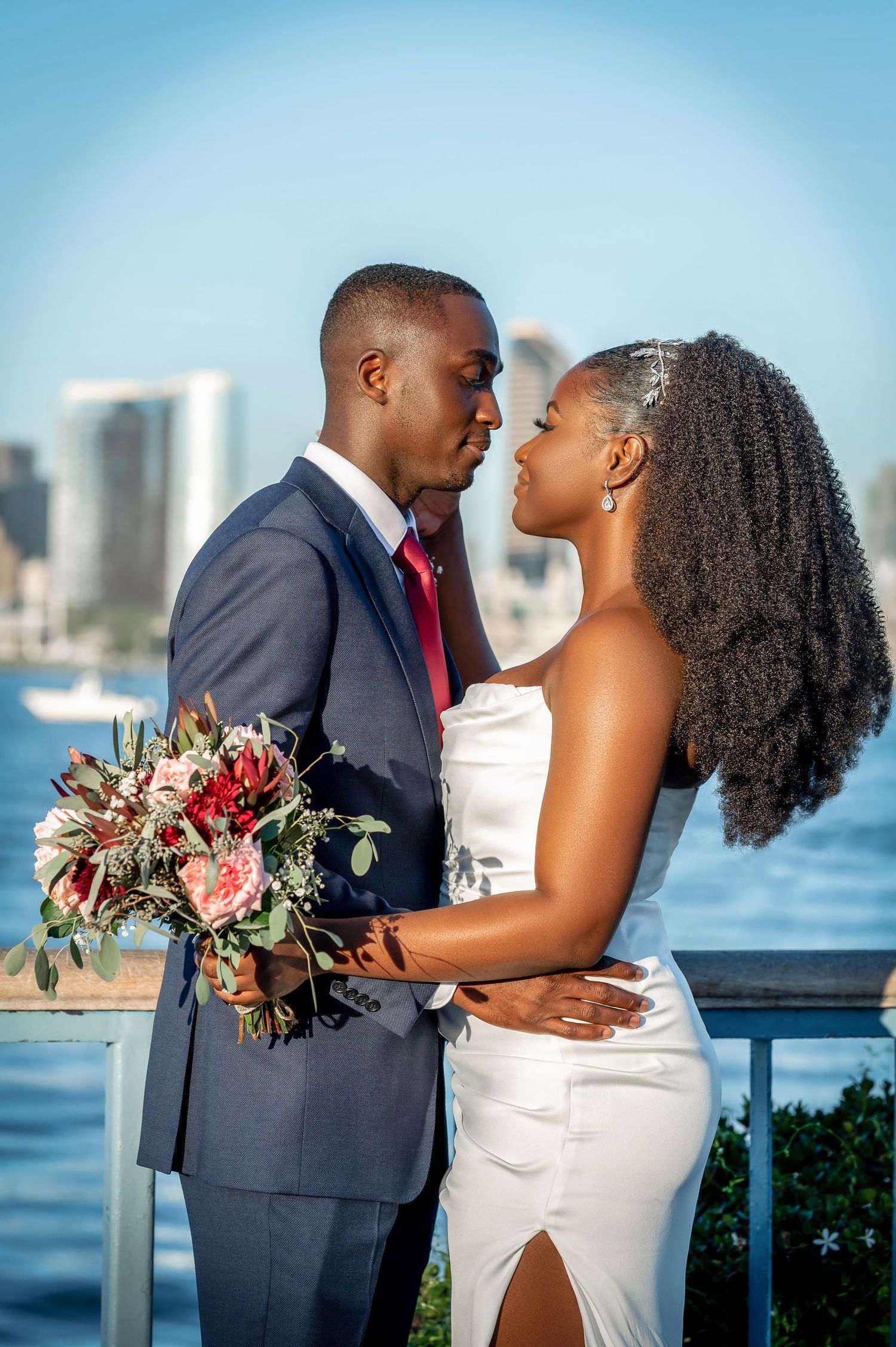 Couple shares intimate moment on waterfront balcony with cityscape background.