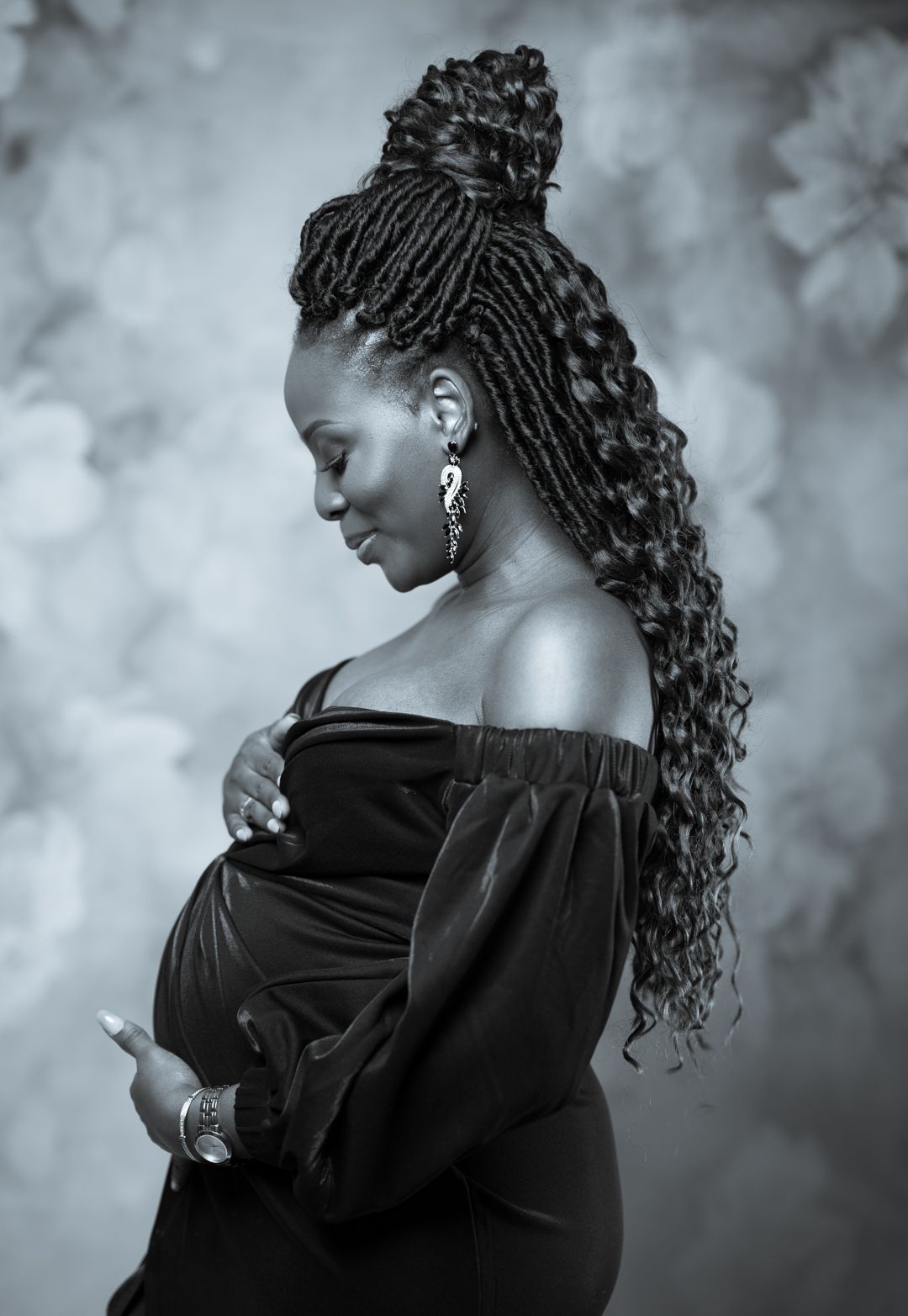 Artistic black and white portrait of someone with elaborate braided hairstyle in off-shoulder dress.