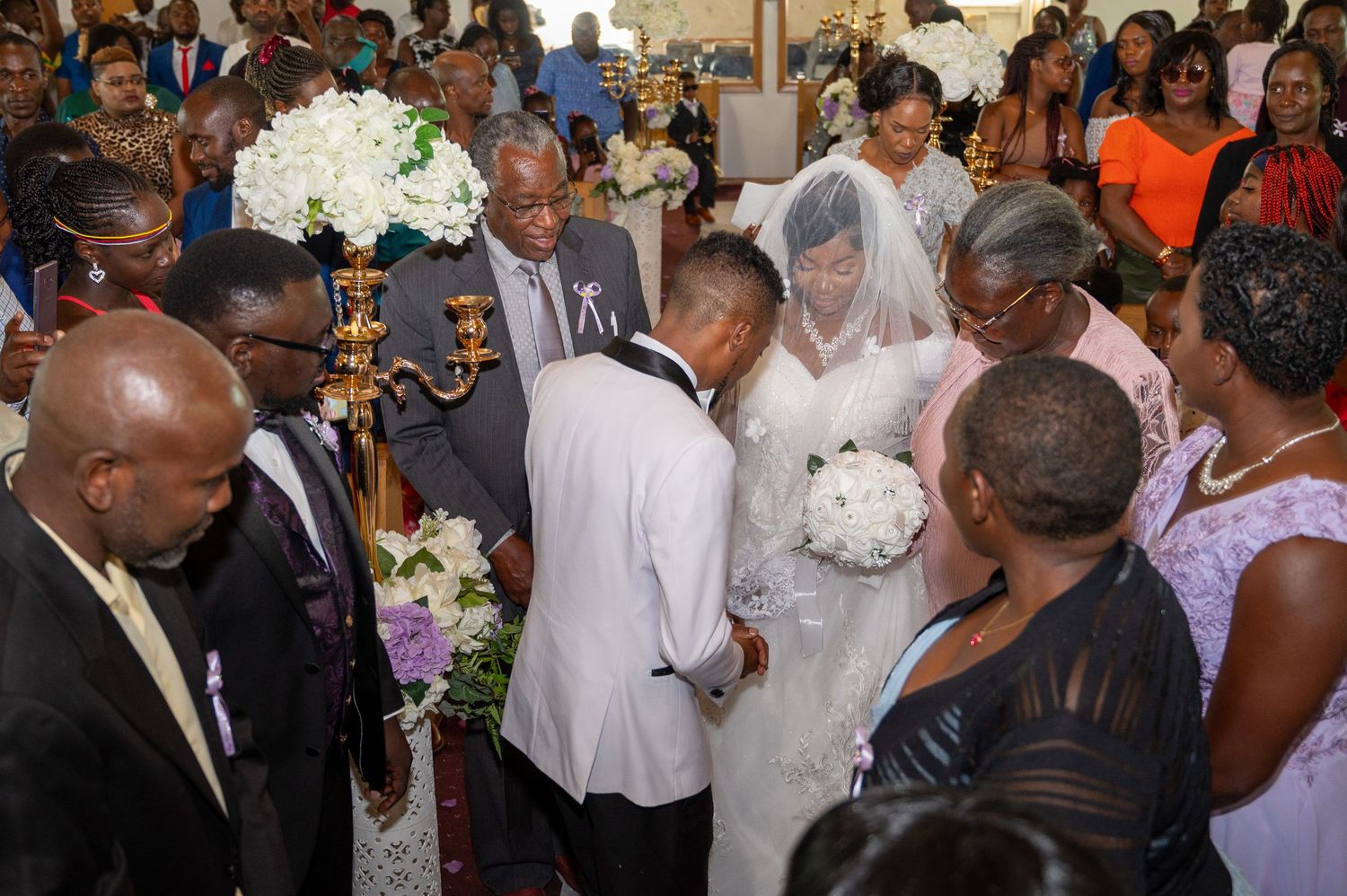 A crowded wedding ceremony with guests gathering around the couple in formal attire.