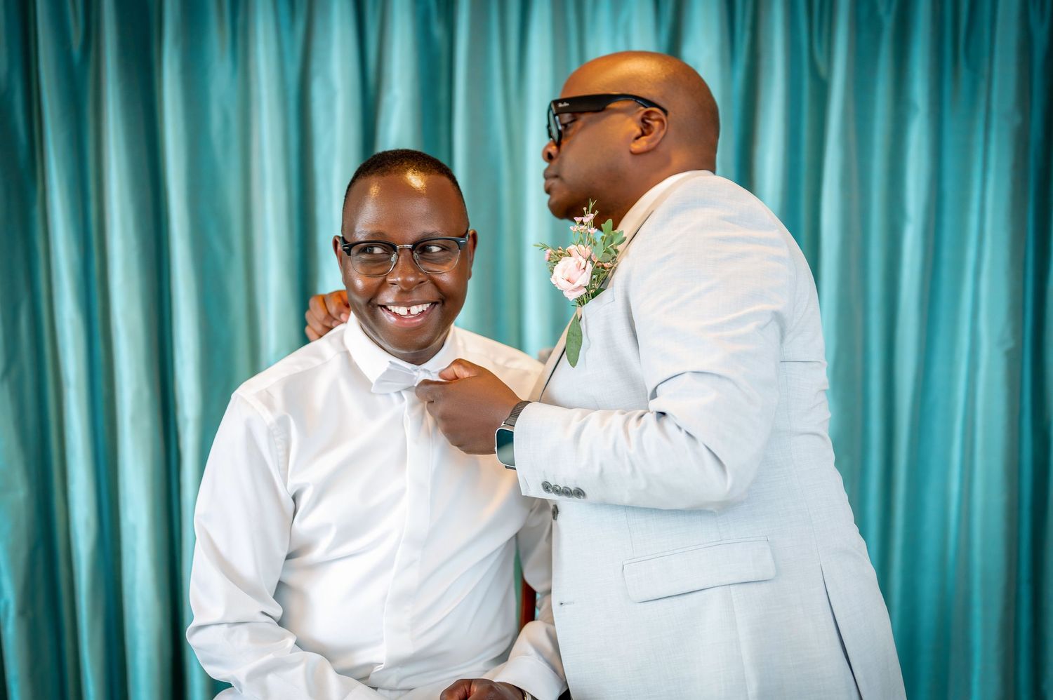 Two people in formal attire sharing a joyful moment against teal backdrop.