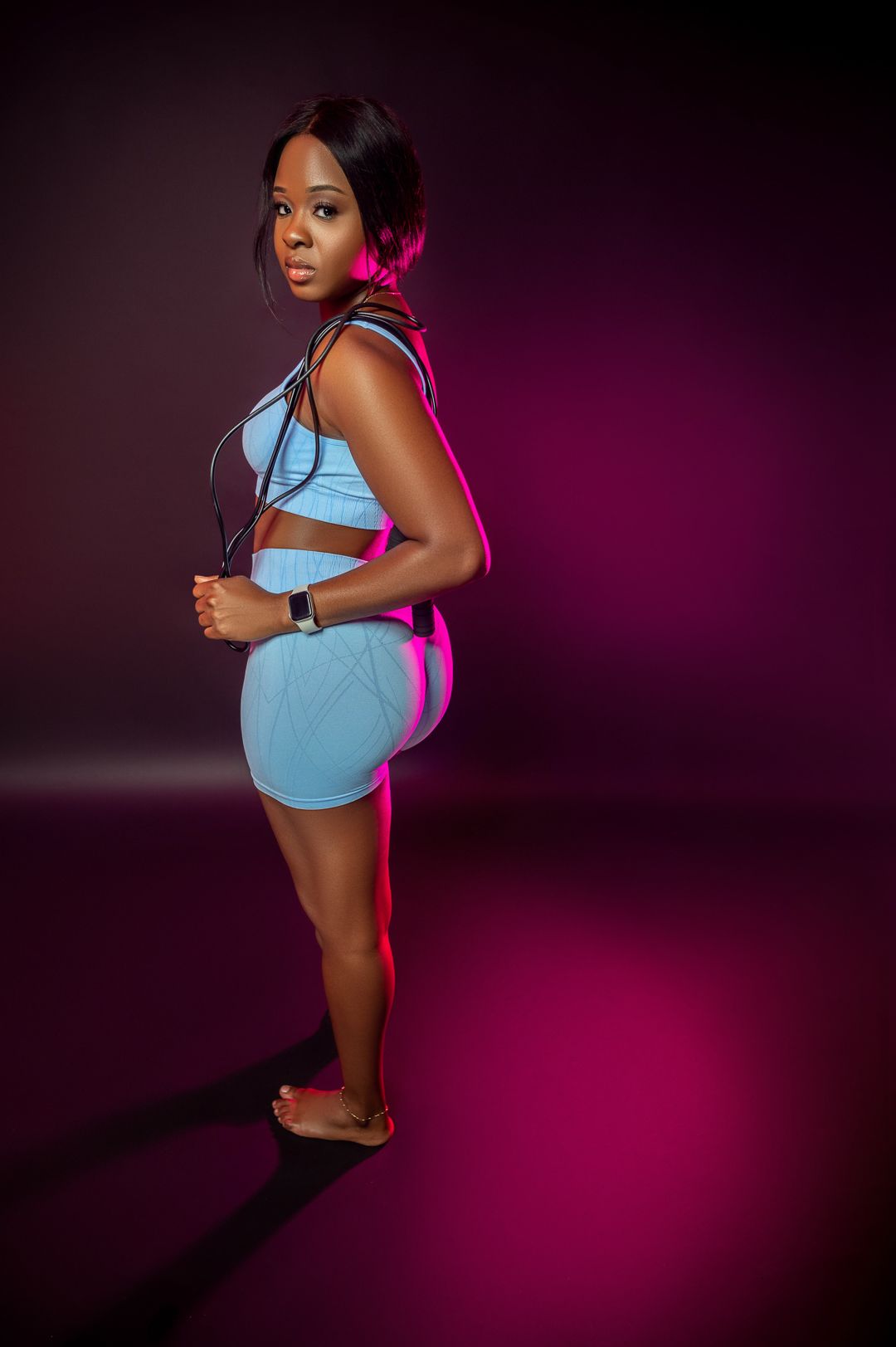 Athletic figure in light blue workout set against dark purple studio background.