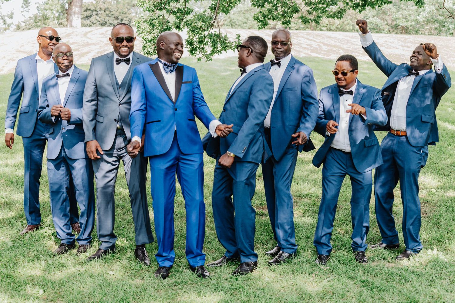 Groomsmen in coordinating blue suits pose playfully for a group photo outdoors.