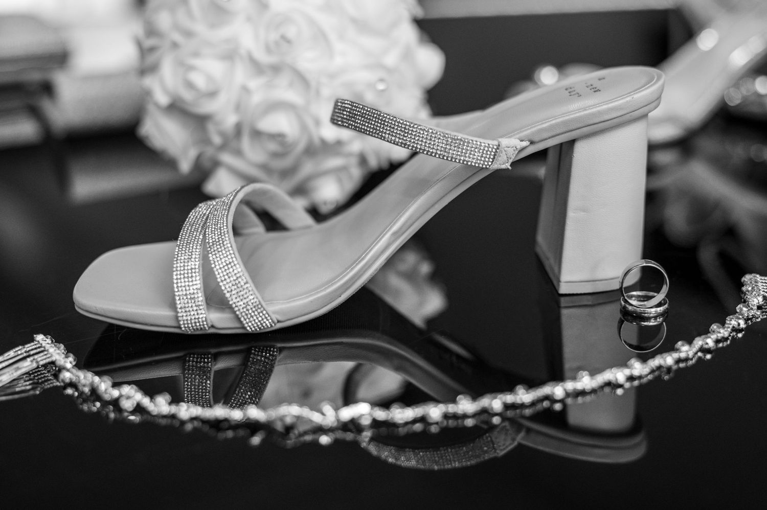Elegant silver strappy sandal with block heel displayed on reflective surface with decorative details.