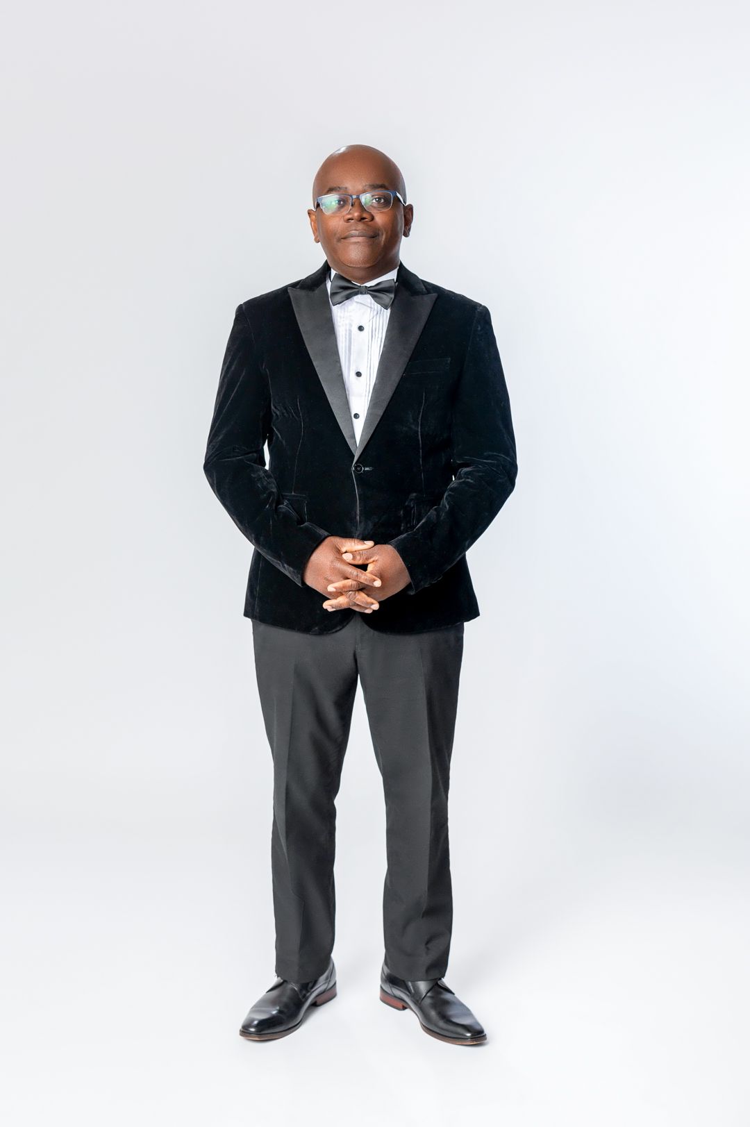 A professional in a black velvet tuxedo jacket and bow tie poses against a white background.