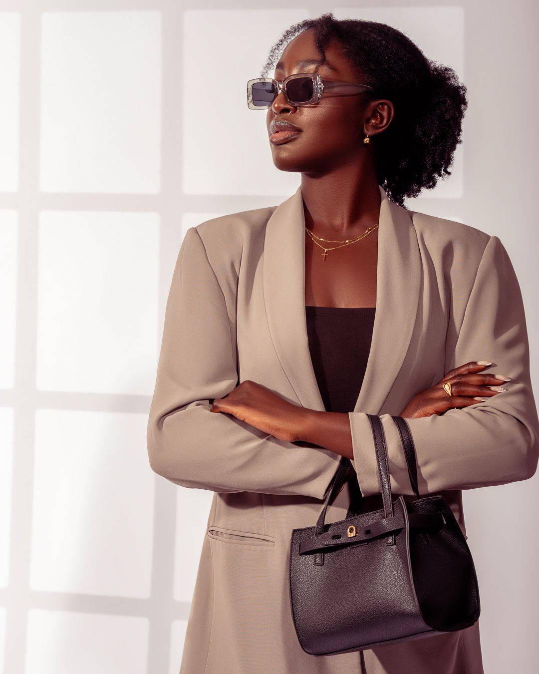 Business chic pose in beige blazer with sunglasses and small black handbag.