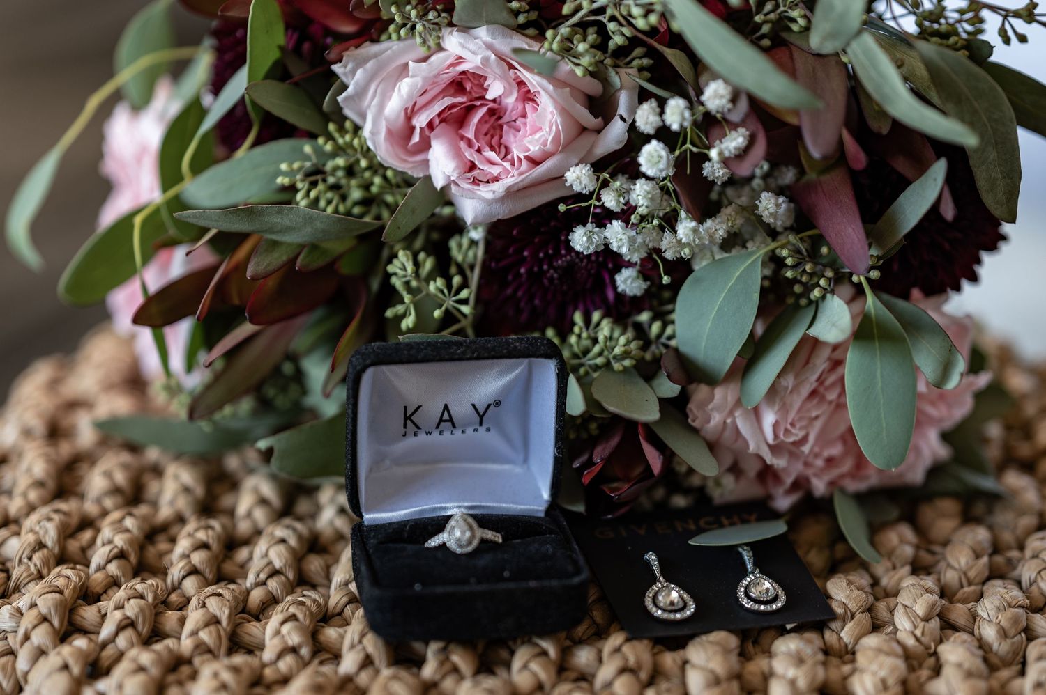 Wedding ring and earrings in black box with pink roses and greenery bouquet.