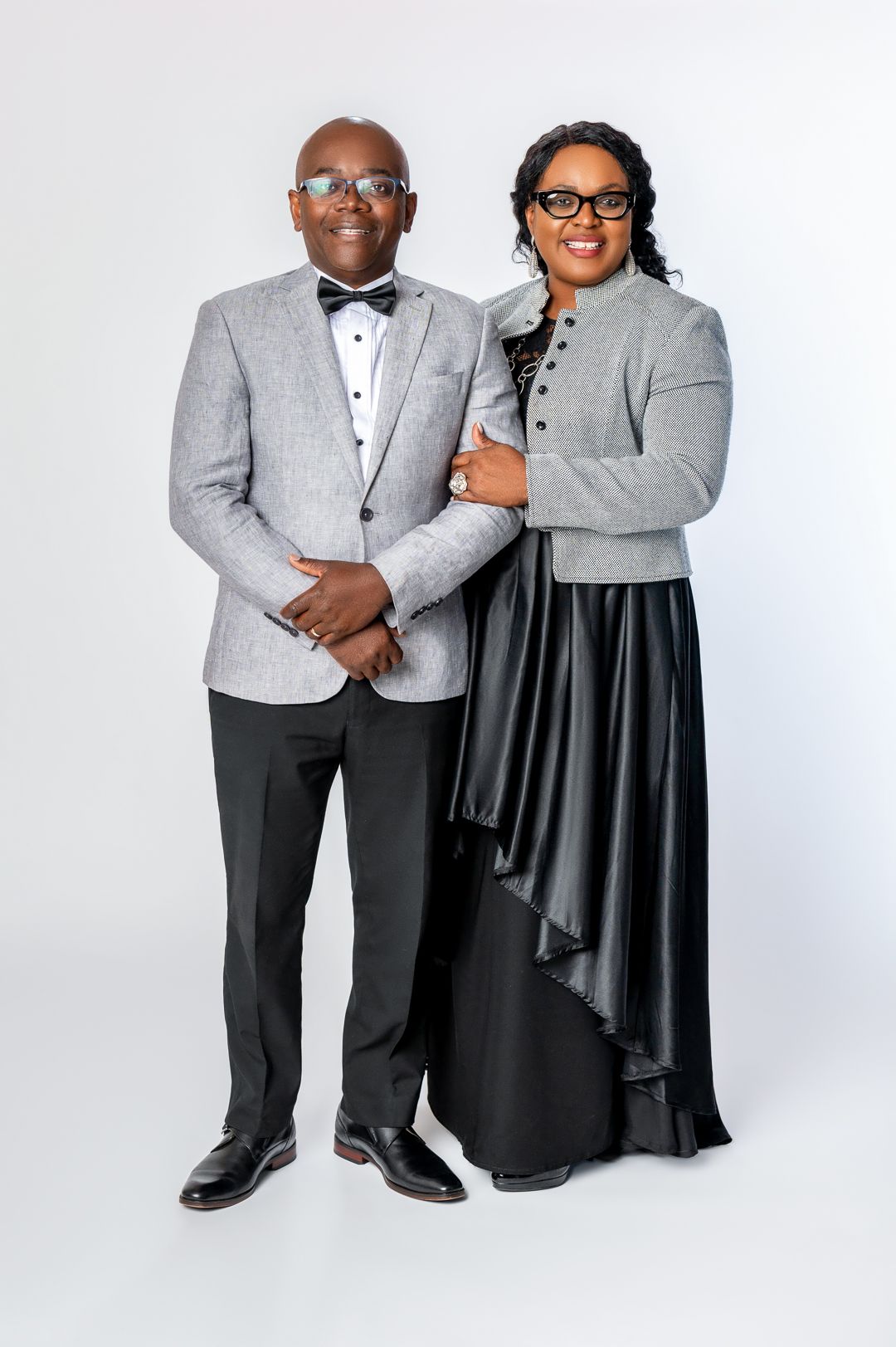 A formal couple's portrait featuring coordinating gray formalwear against white background.