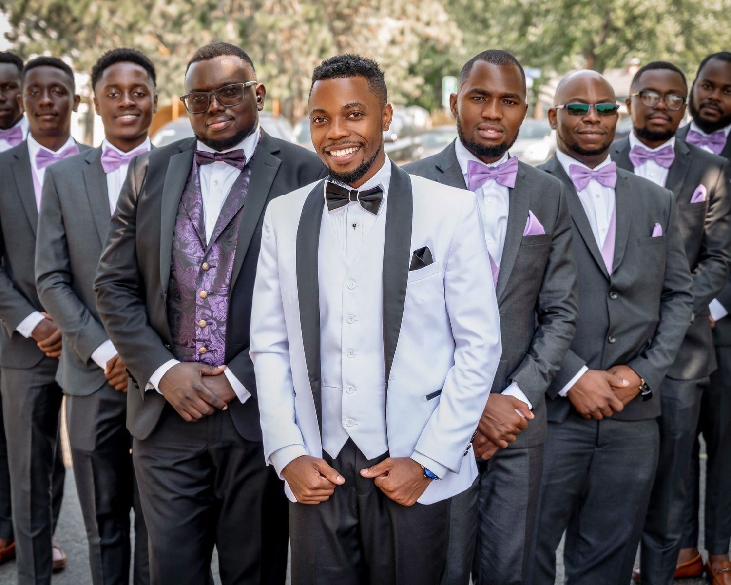Groomsmen in stylish suits and bowties pose together outdoors for wedding photo.