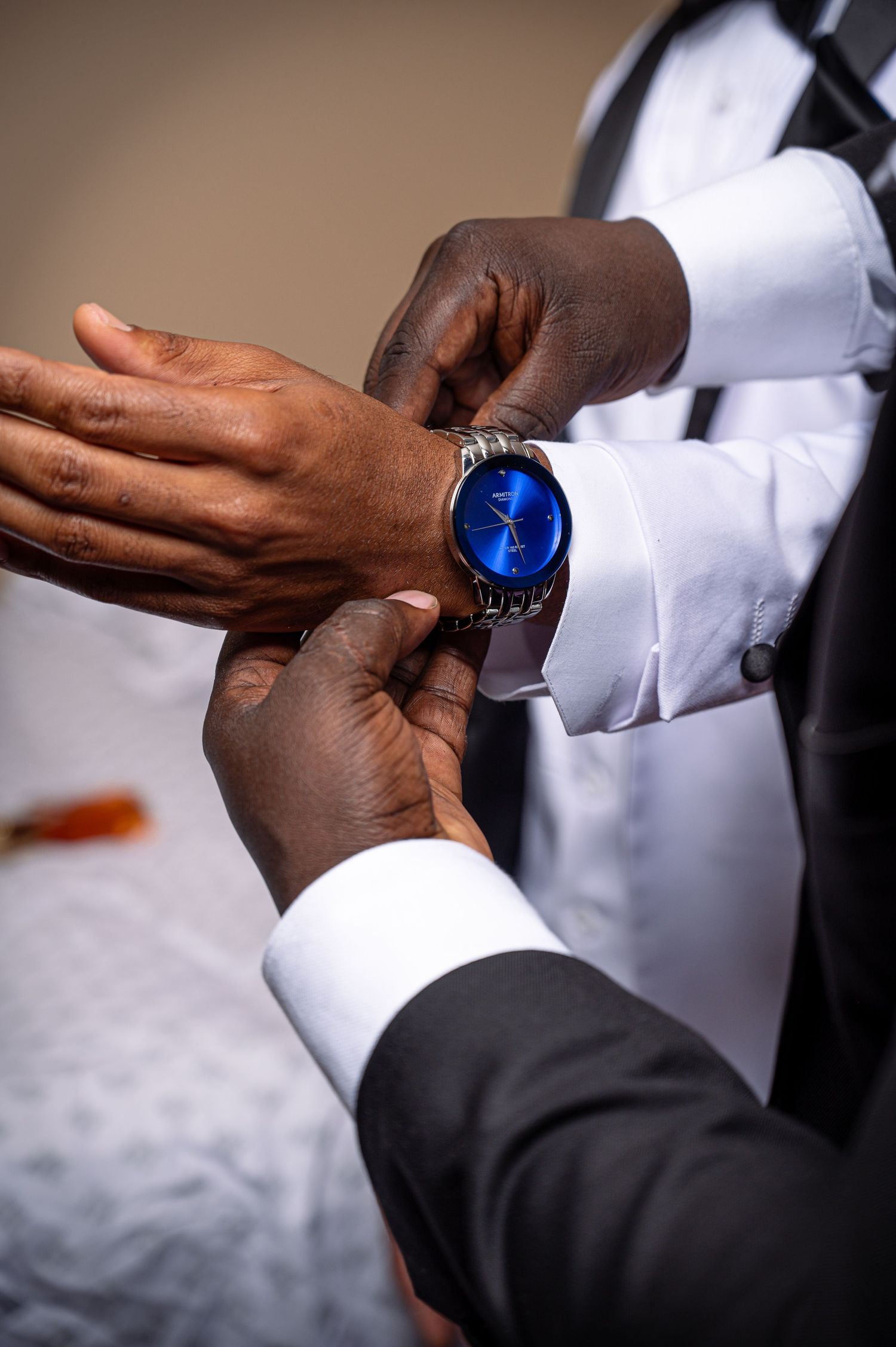 Close-up of hands adjusting a stylish blue watch face on formal attire.