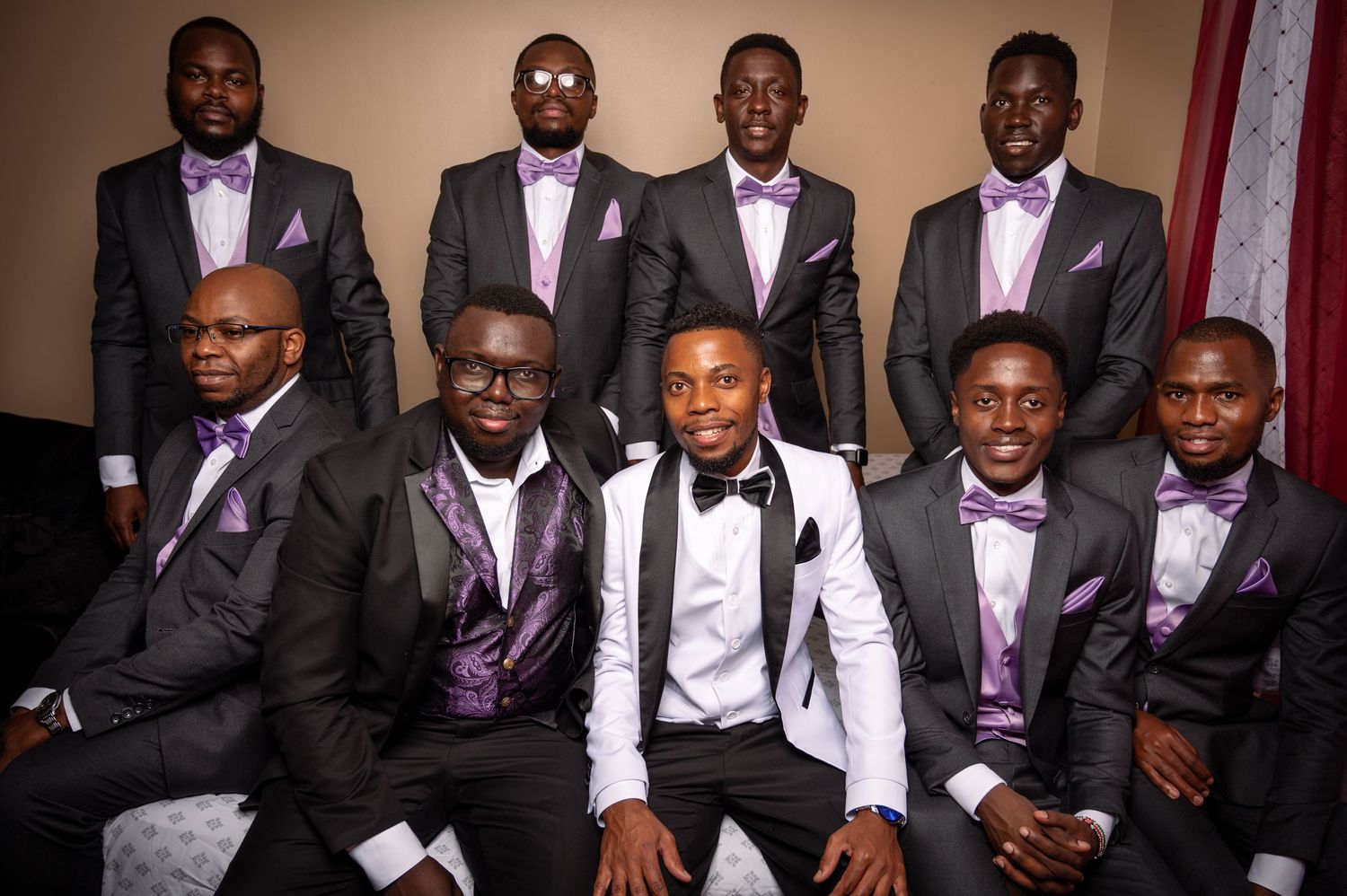 Groomsmen in matching purple and black formal attire pose for a wedding photo in two rows.