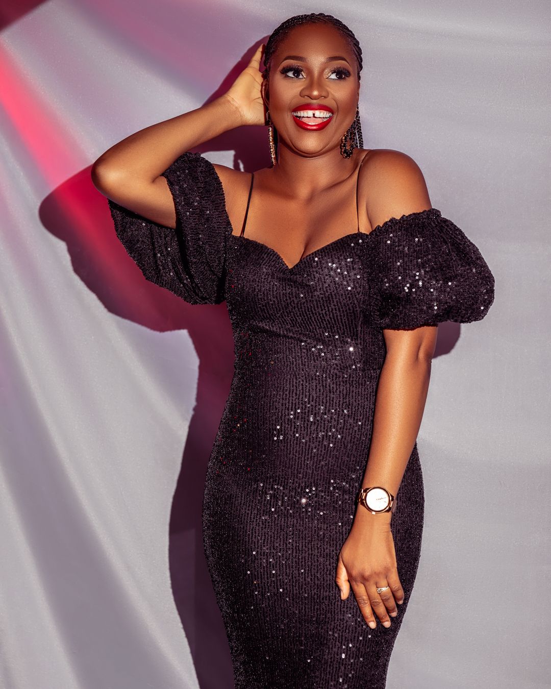 Glamorous pose in black sequined dress with puff sleeves against soft draped background.