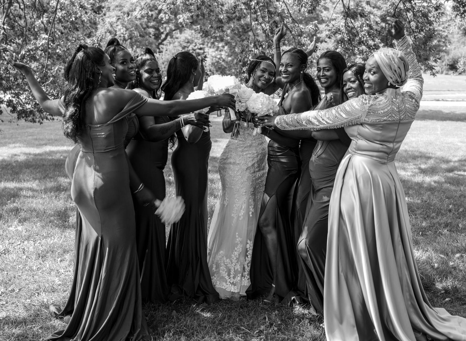 Bridal party in flowing dresses forms a circle outdoors during wedding celebration.