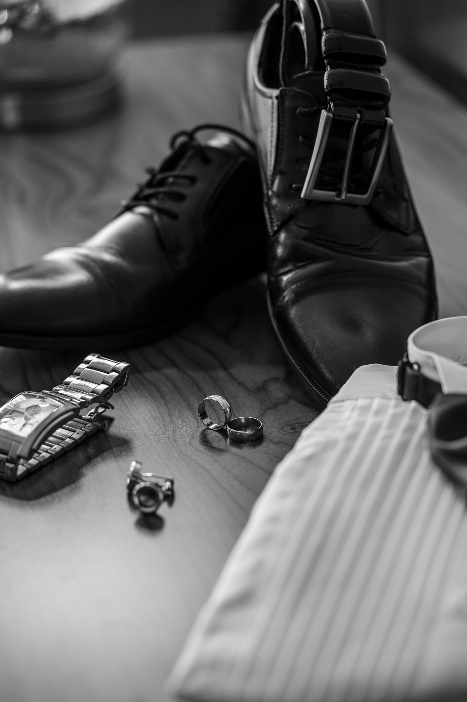 Black formal shoes, belt, and accessories arranged for wedding preparation.