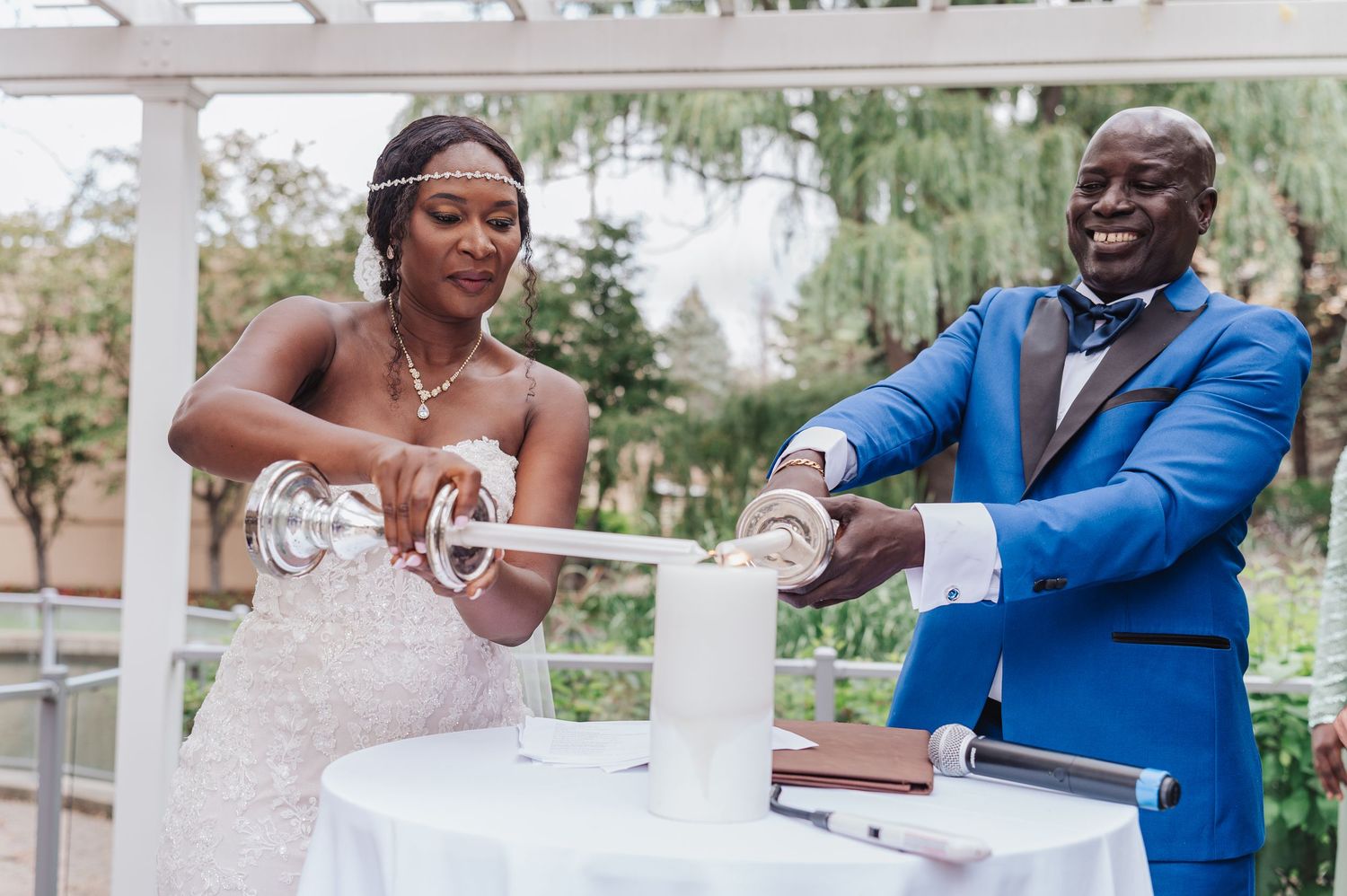 A couple performs a unity candle ceremony during their outdoor garden wedding.