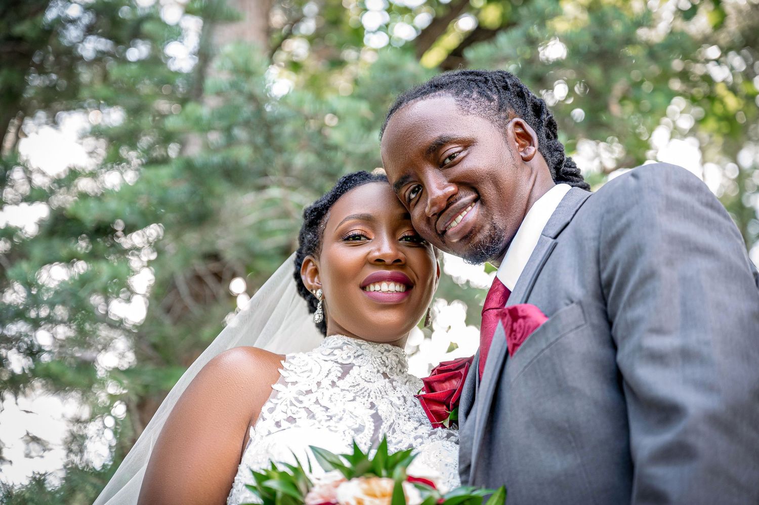 A joyful couple embraces outdoors in wedding attire with a bouquet of flowers.