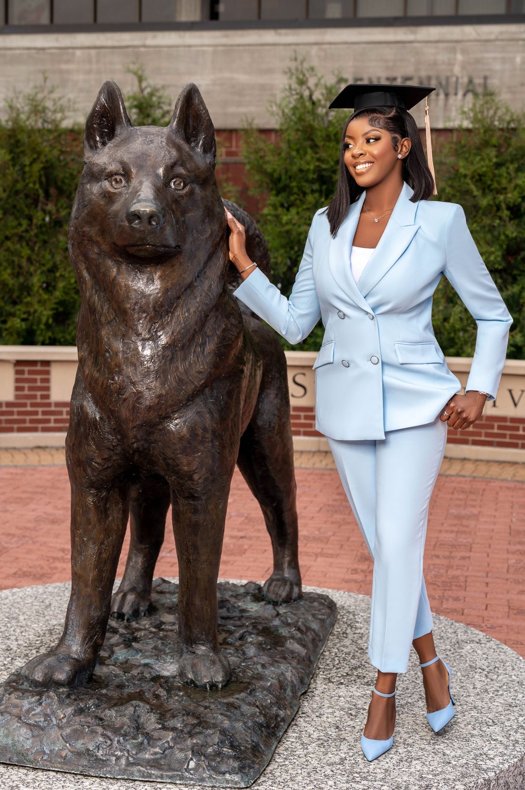 Graduate in powder blue suit poses with university mascot wolf statue.