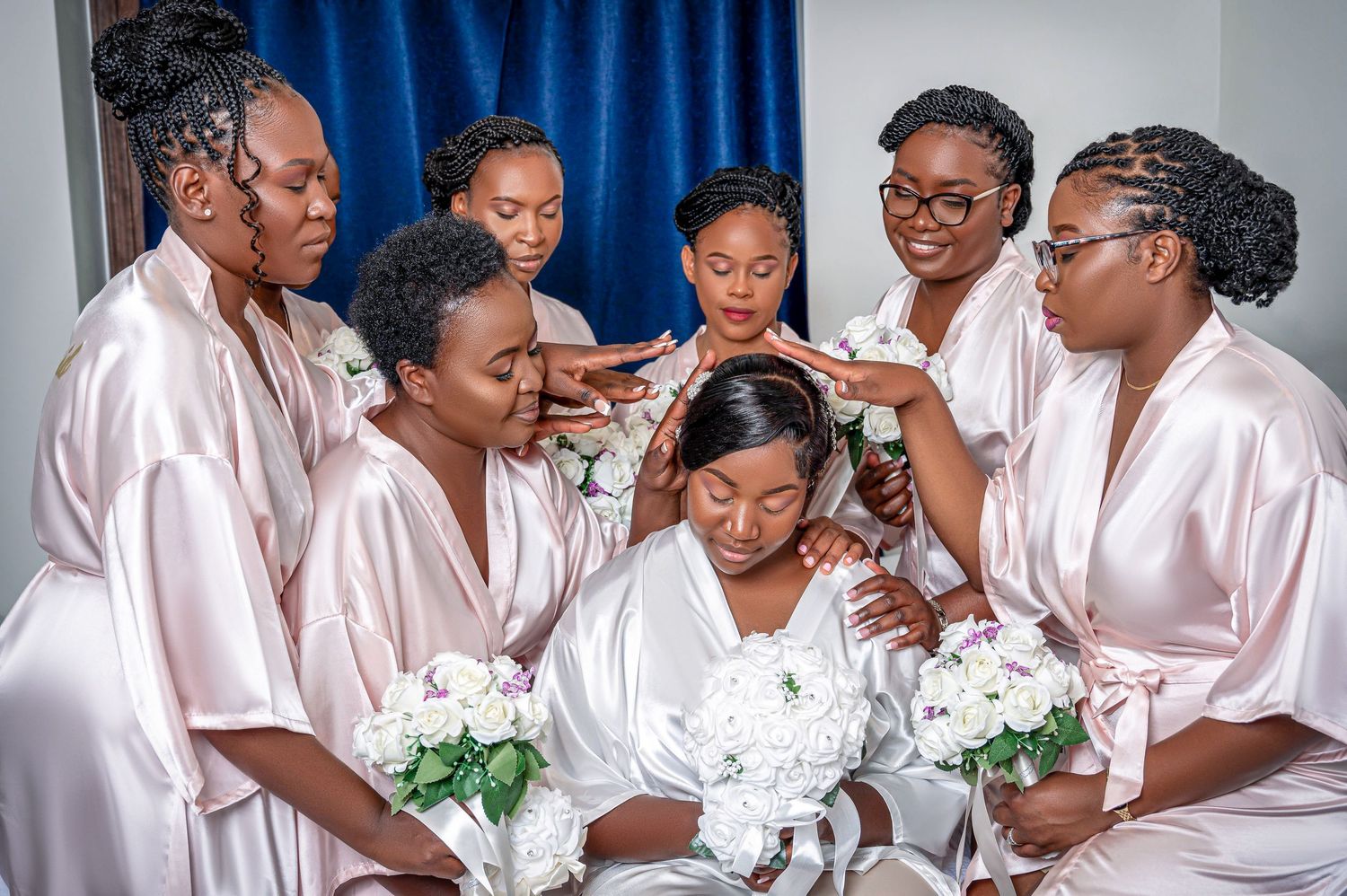 Bridal party in pink satin robes gathered around bride during wedding preparations.