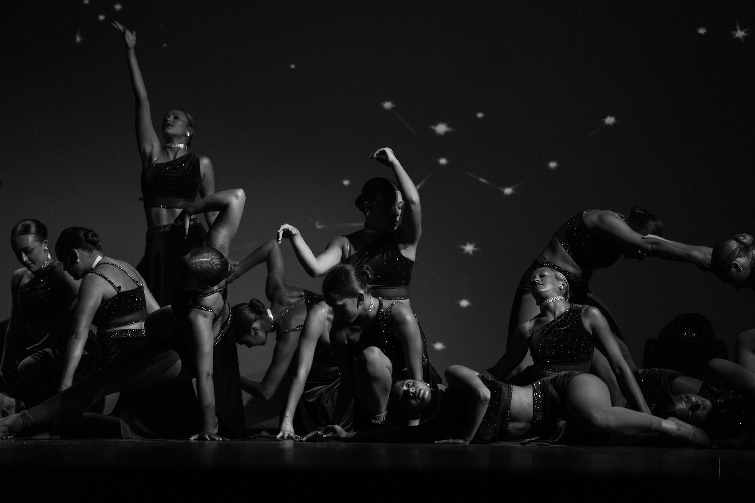 Black and white photo of dancers performing on stage with dramatic poses and spotlights in the background.