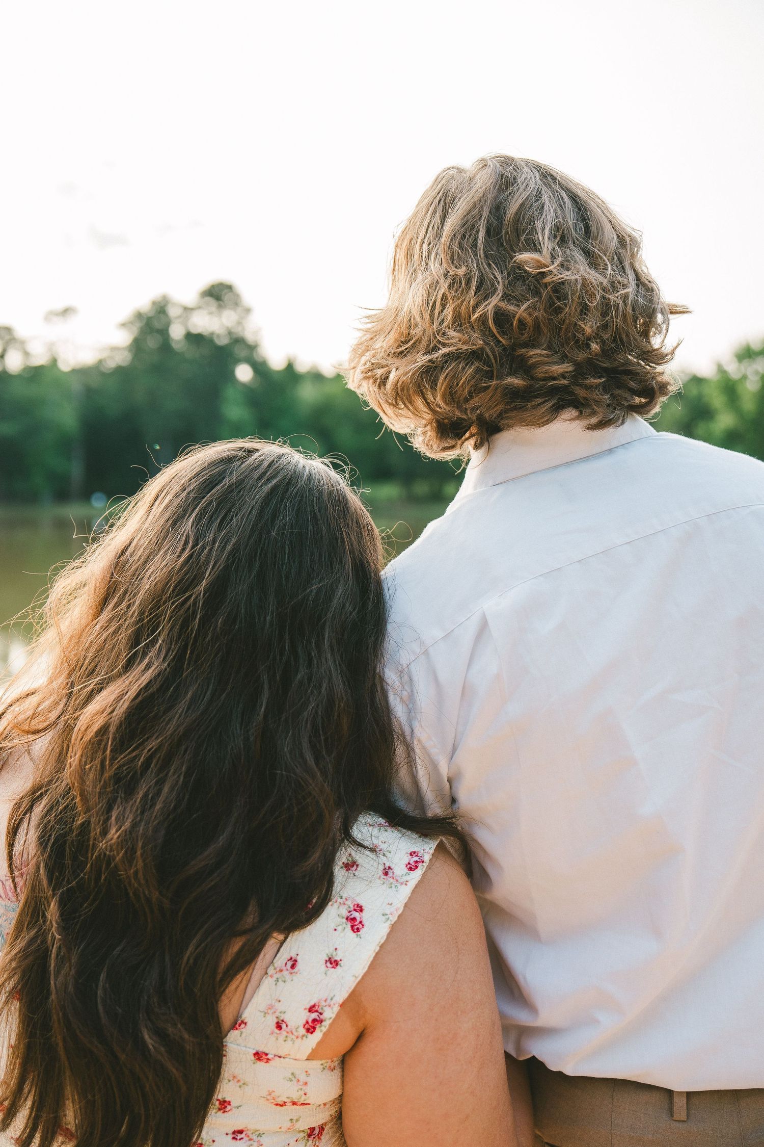 Couple in casual attire embracing while viewing sunset by lake.